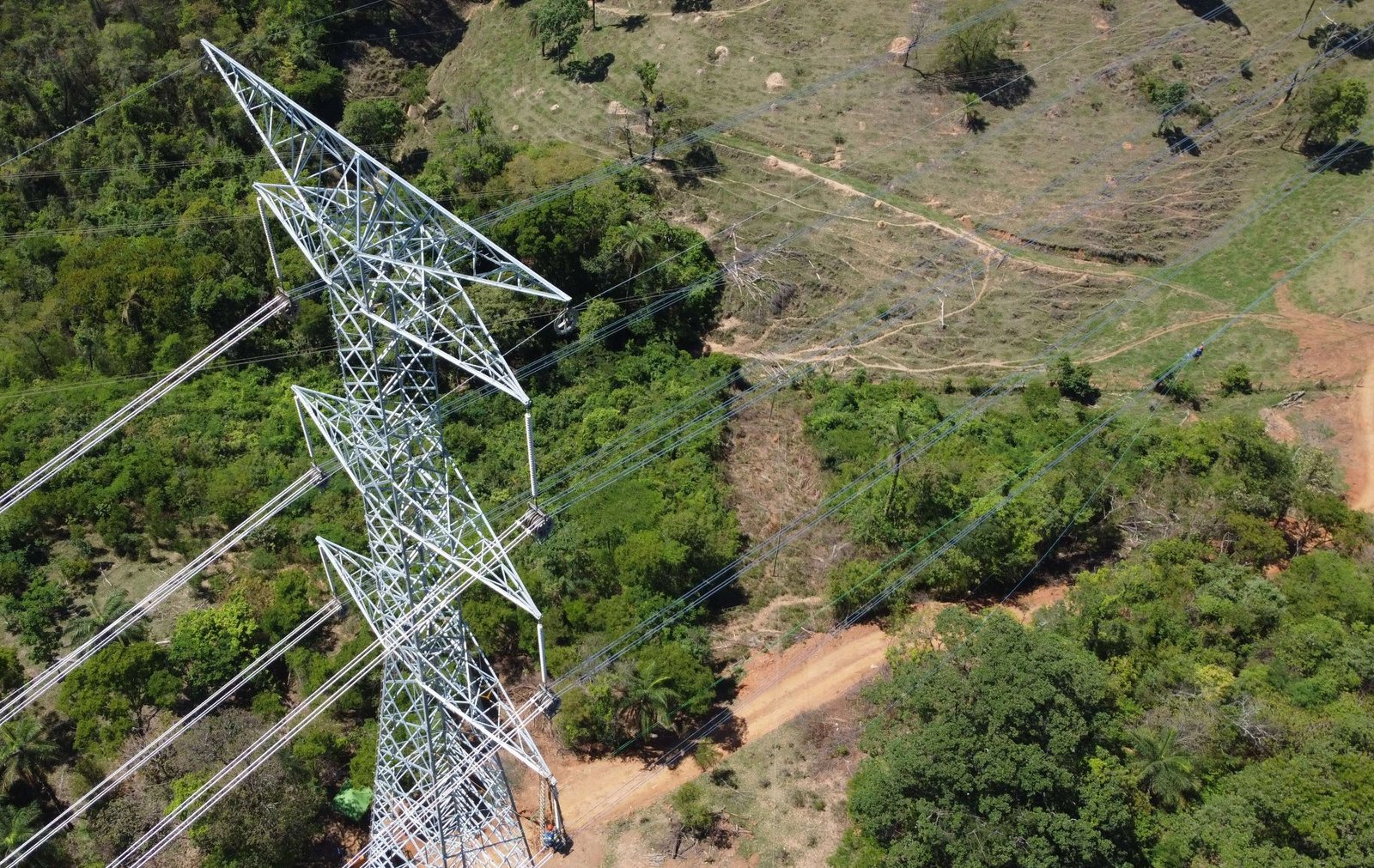 Vista aérea dramática de torre de Linha de Transmissão em meio a floresta densa, durante lançamento de cabo com drone