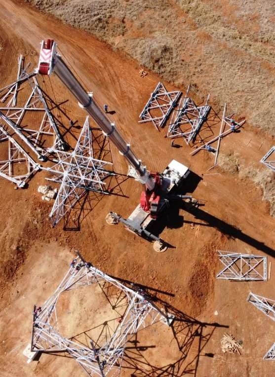 Vista aérea de guindaste montando estrutura de torre de Linha de Transmissão em terreno de terra vermelha